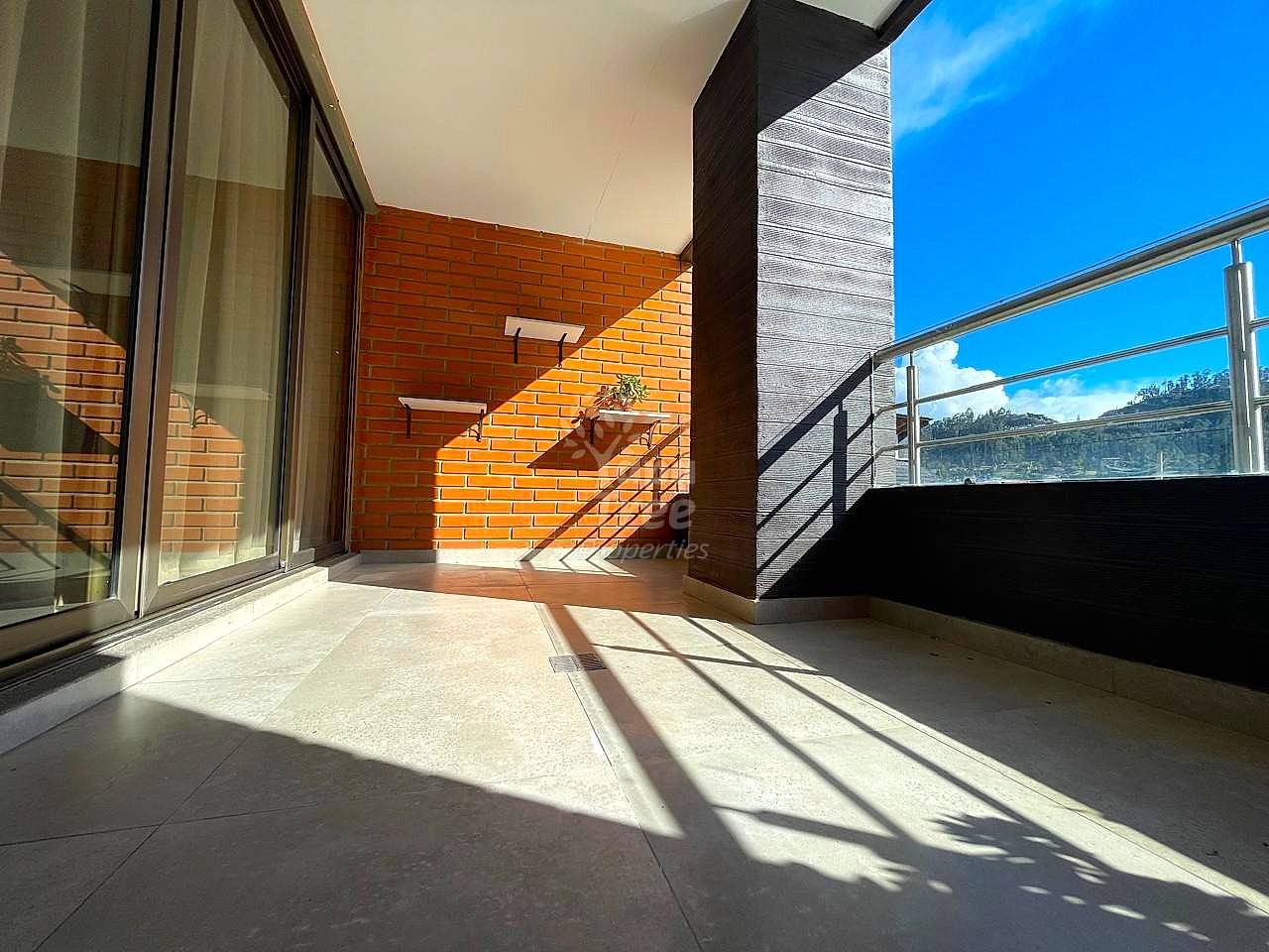 Covered terrace with tile flooring, orange brick wall, metal railing, and glass sliding doors opening to interior space with mountain views.