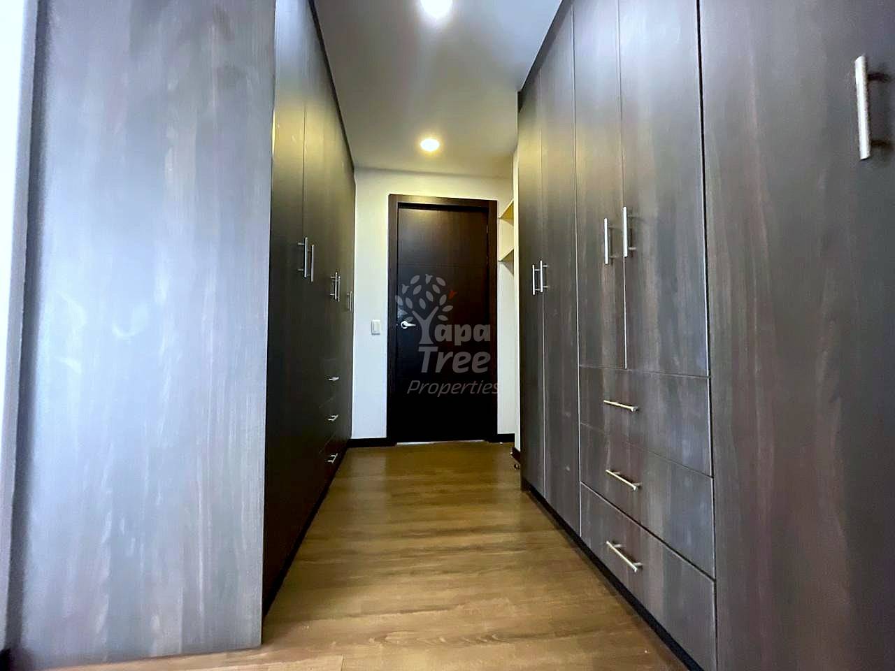 A narrow hallway or walk-in closet with dark wood wardrobes on both sides and light wooden floors.