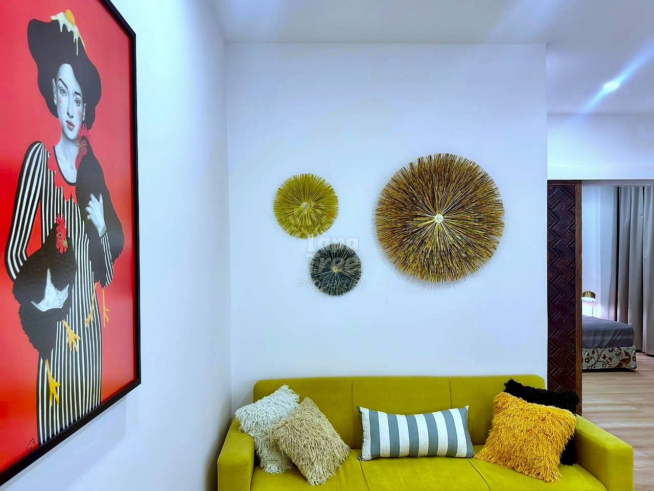 Living room with yellow sofa, decorative woven wall discs, pop art portrait on red panel, and wooden flooring.