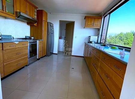 Galley cocina with wooden cabinetry, stainless steel stove and refrigerator, tiled floors, and large window with outdoor view.