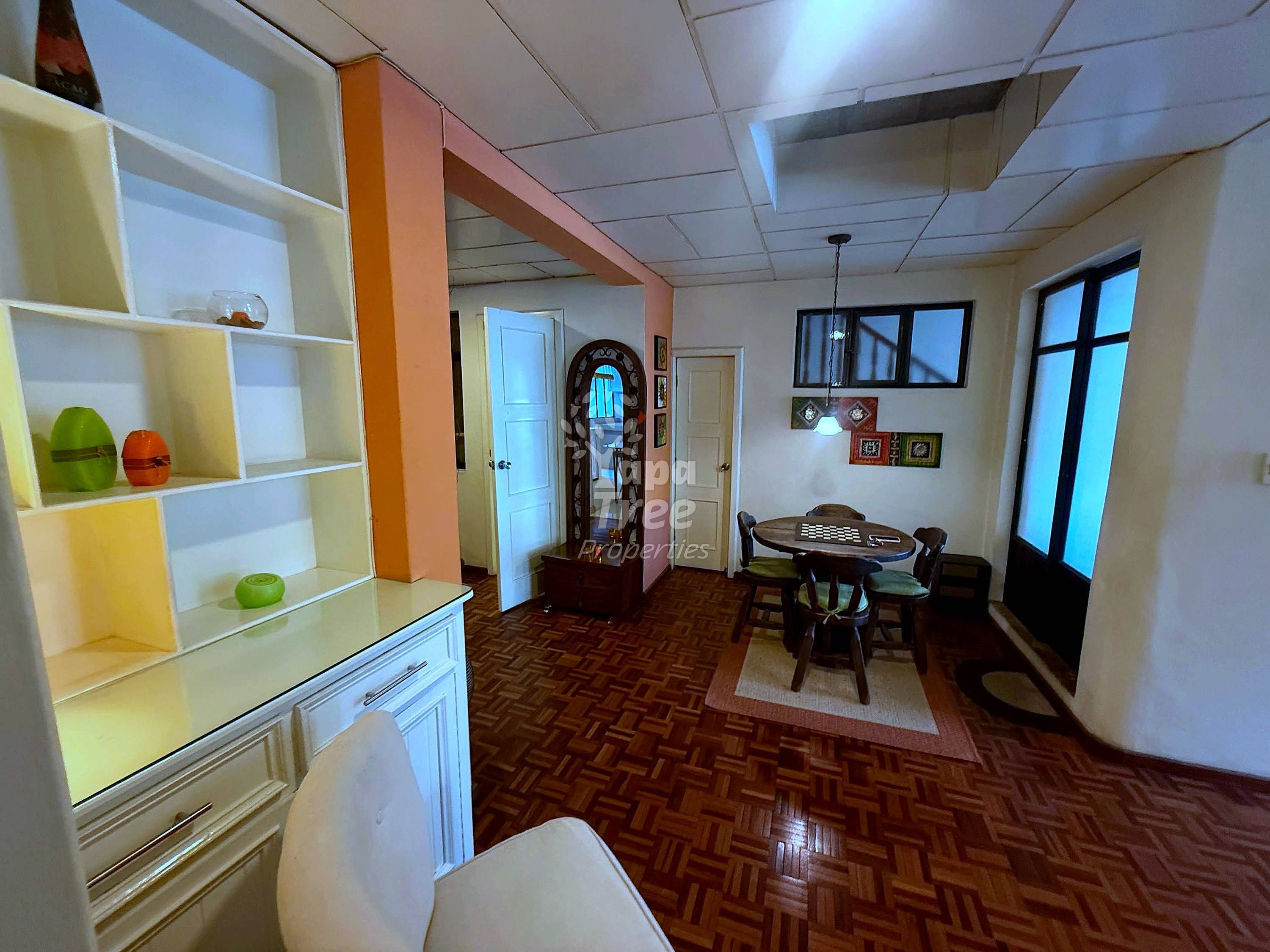 Living room with cream shelving unit, orange accent column, dark wood furniture, herringbone floor, and glass doors with natural light from windows.