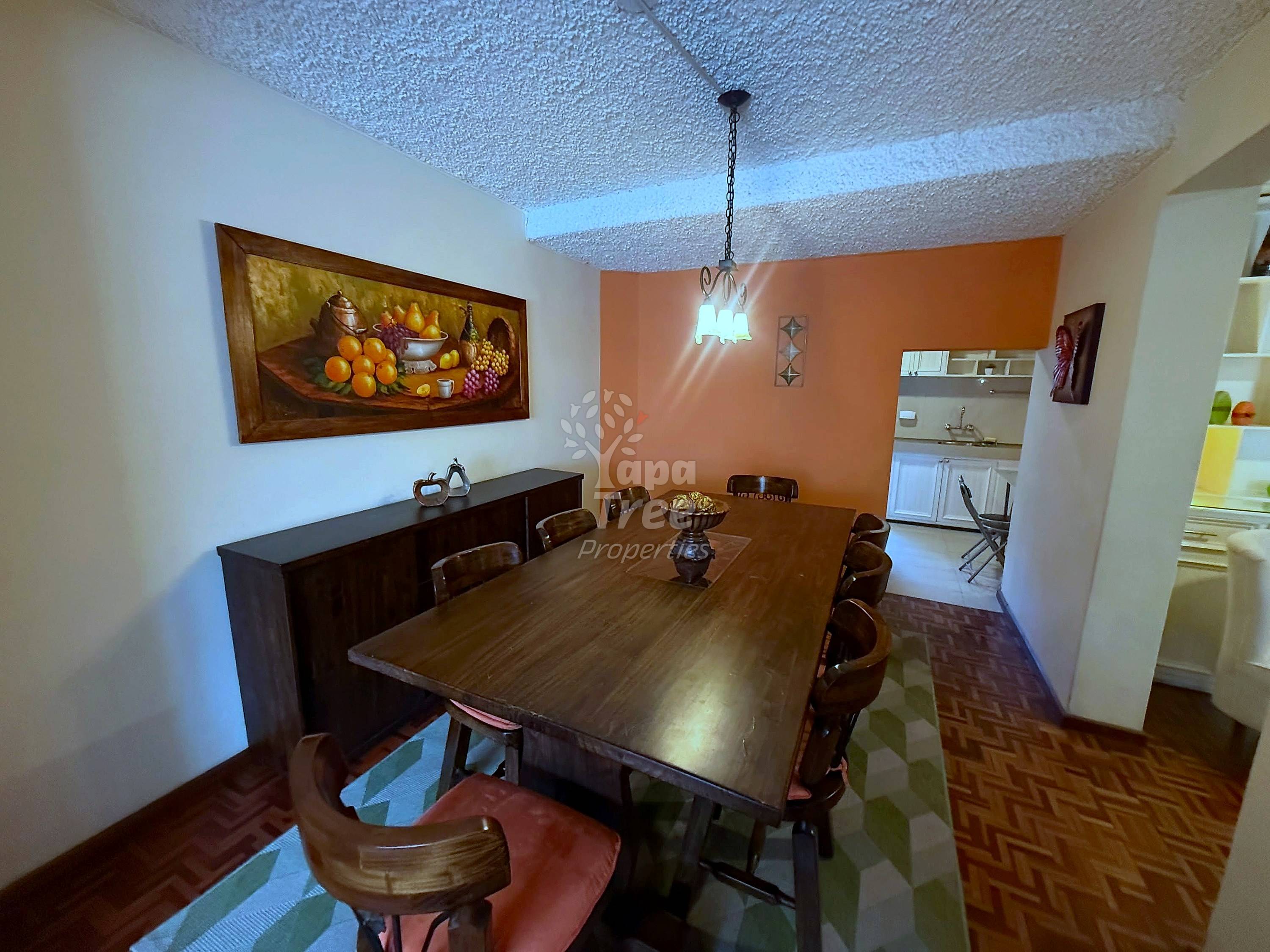 Dining room with wooden table, brown leather chairs, textured ceiling, orange accent wall, and open kitchen visible in background.