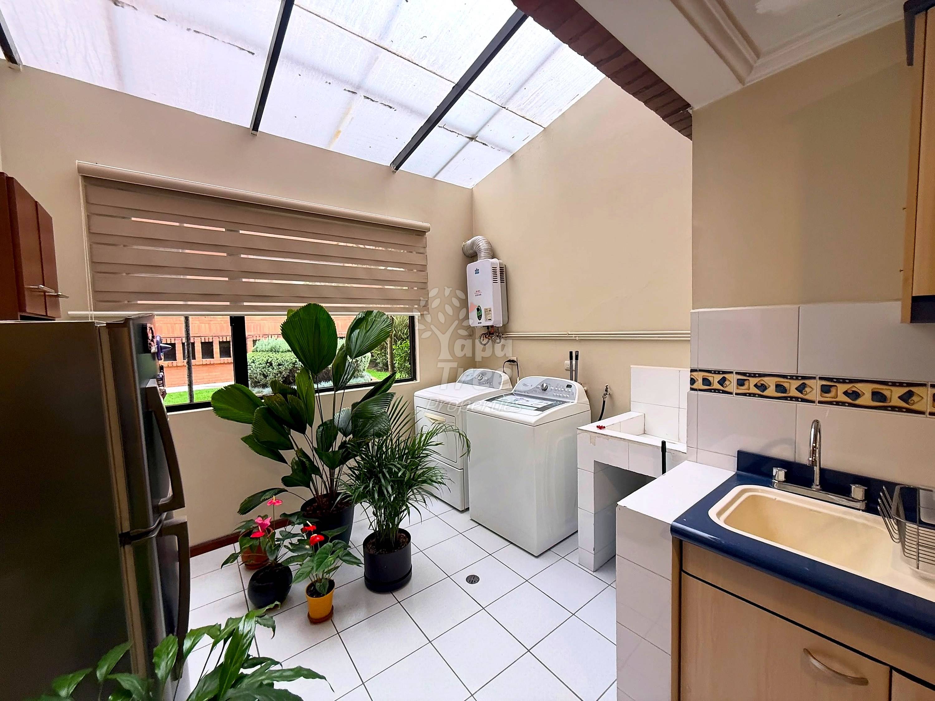 Lavandería with white tile floor, washing machine, sink with navy trim, refrigerator, skylight, and potted plants near window.