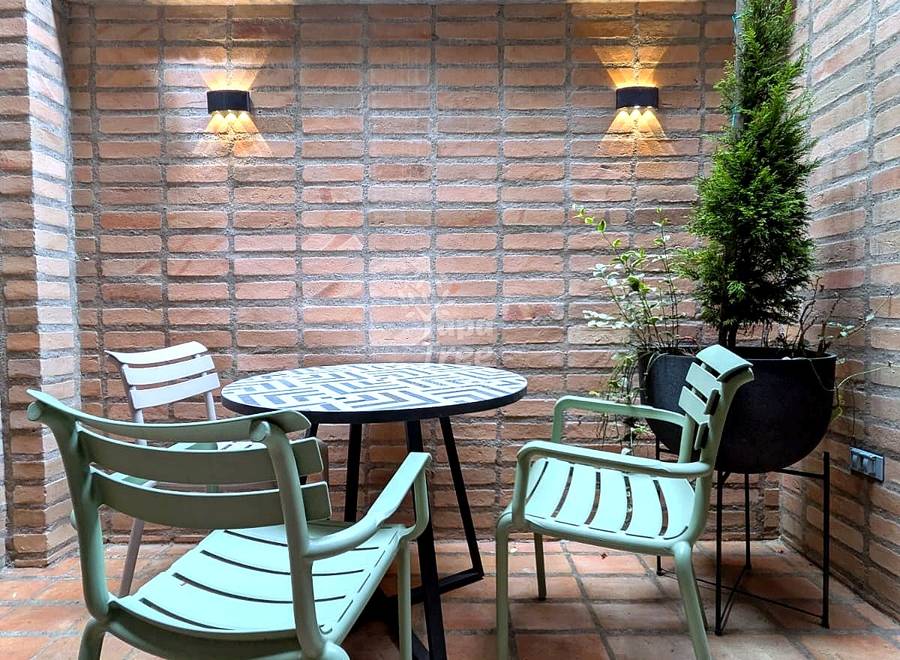 Brick patio with round table, four green chairs, terracotta floor, two wall sconces, and potted plants.