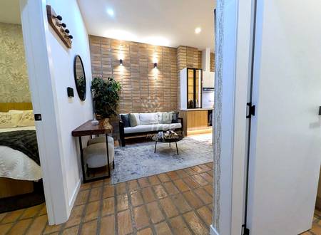 Open-concept suite with terracotta tile floor, sofa with cushions, round mirror, console table, and exposed brick accent wall with warm lighting.