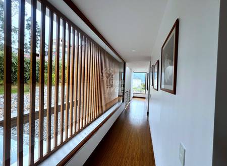 Hallway with dark wood flooring, white walls, vertical dark wood railing with glass panels on left side, framed artwork on right wall, natural light from windows.