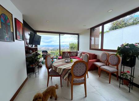 Living room with dining table, wooden chairs, red sofa, TV, large windows overlooking valley, recessed ceiling lights, tile flooring.