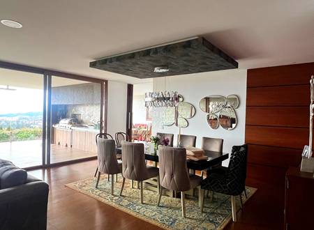 Dining room with black table, gray upholstered chairs, dark wood accent wall, recessed ceiling light fixture, and glass doors opening to terrace with valley views.