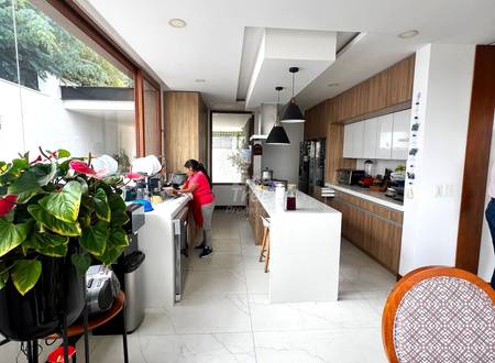 Modern kitchen and dining area with white marble flooring, wood cabinetry, white countertops, black pendant lights, and large windows with natural daylight.