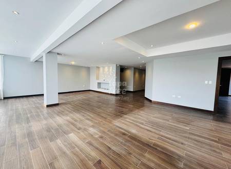 Open-concept living area with wood-grain floor, white columns, recessed ceiling lights, and white walls with doorway access.