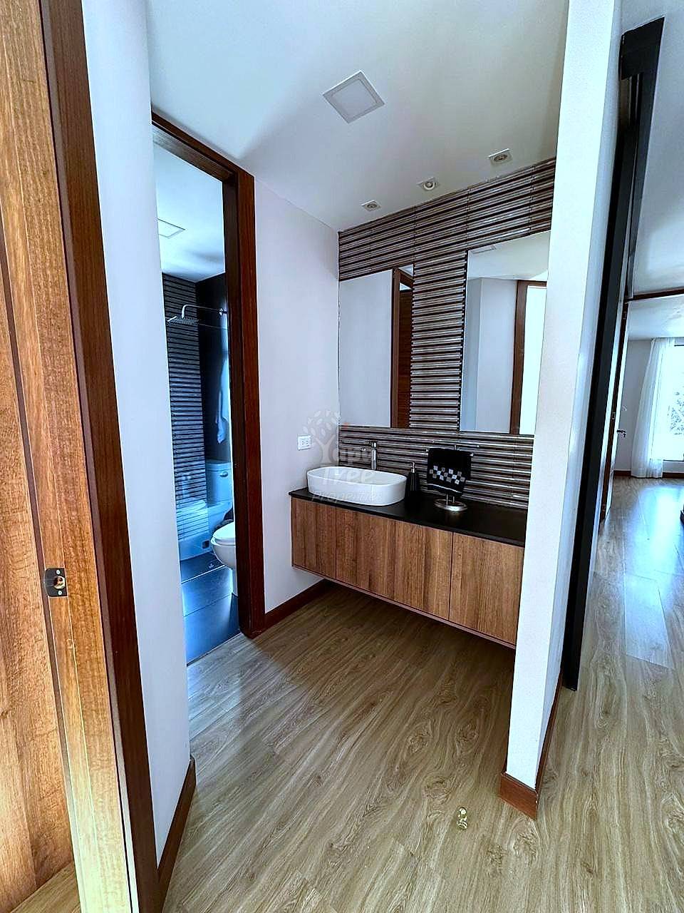 Bathroom with wood-grain flooring, white vessel sink on dark counter, wood vanity cabinet, striped tile backsplash, and mirror with separate toilet room.