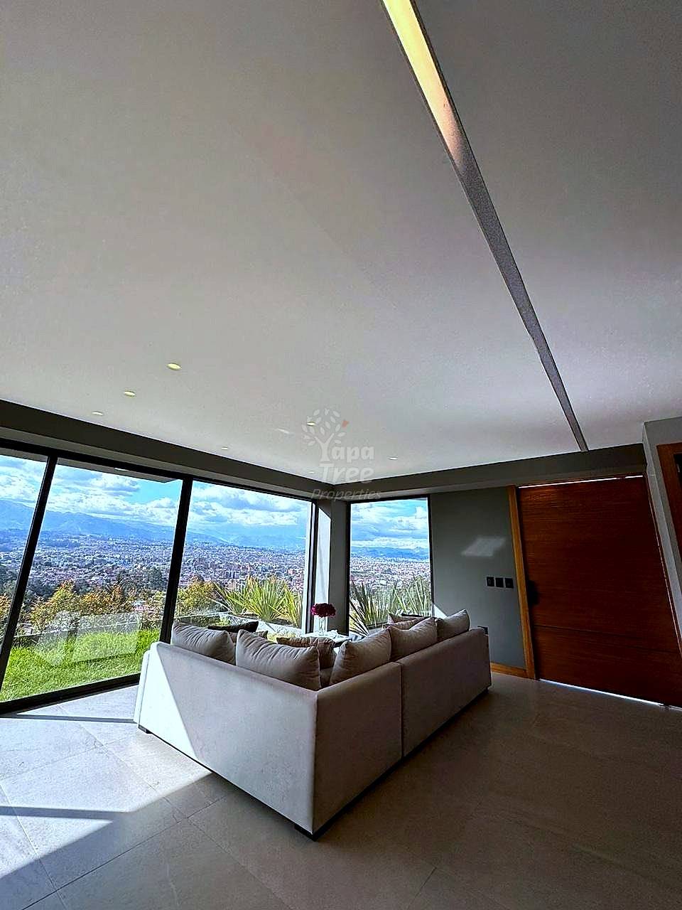 A modern living room with a cream sofa and panoramic city views from large windows.