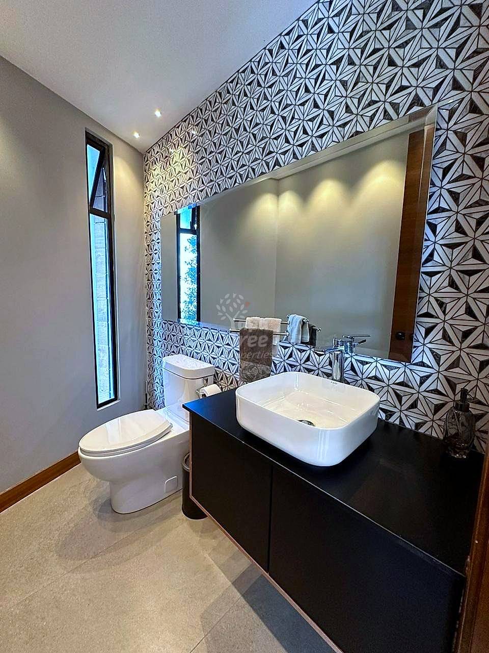 Modern bathroom with geometric patterned wallpaper, white rectangular vessel sink on black vanity, toilet, large mirror, and recessed lighting.