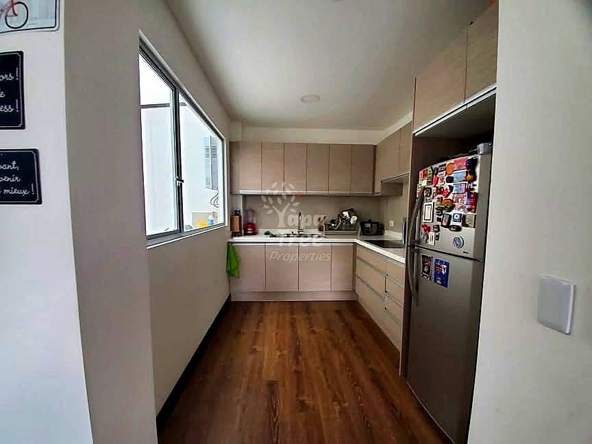Narrow galley cocina with beige cabinetry, stainless steel refrigerator, dark wood flooring, and window with natural light.