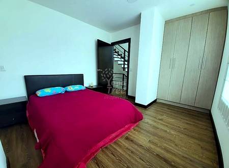 Dormitorio con cama queen cubierta en ropa de cama roja, cabecero negro, armario de madera, puerta metálica negra con vista a escaleras, piso de madera, paredes blancas.