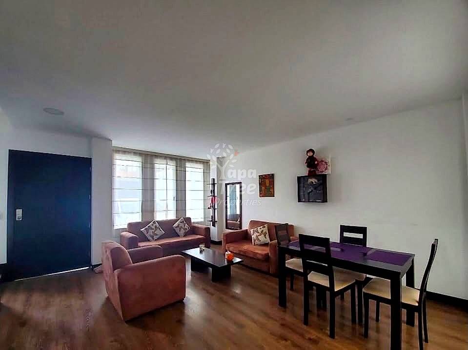 Living room with burgundy leather sofa and armchair, black dining table with chairs, wooden floor, and large windows with sheer curtains