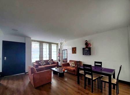 Sala de estar con sofá y sillón de cuero color vino, mesa de comedor negra con sillas, piso de madera y ventanales grandes con cortinas translúcidas