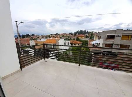 Balcón con piso de cerámica gris claro, barandal de metal oscuro, con vista al barrio de Cuenca con edificios residenciales variados y cielo nublado.