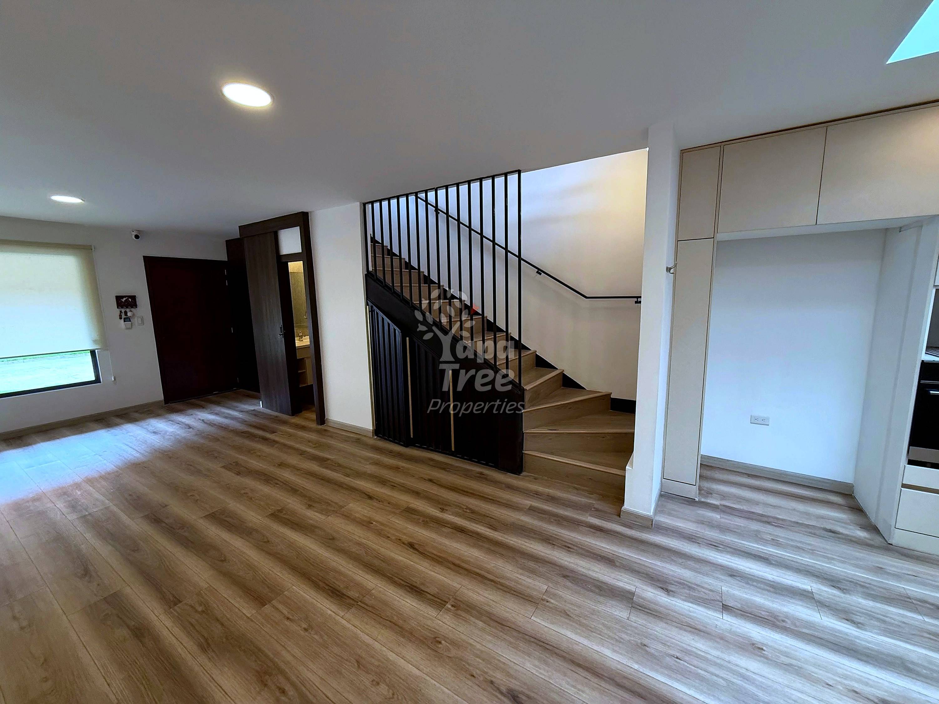 Open-plan living area with wood-look laminate flooring, staircase with black metal railings, recessed ceiling lights, and white built-in closet doors.