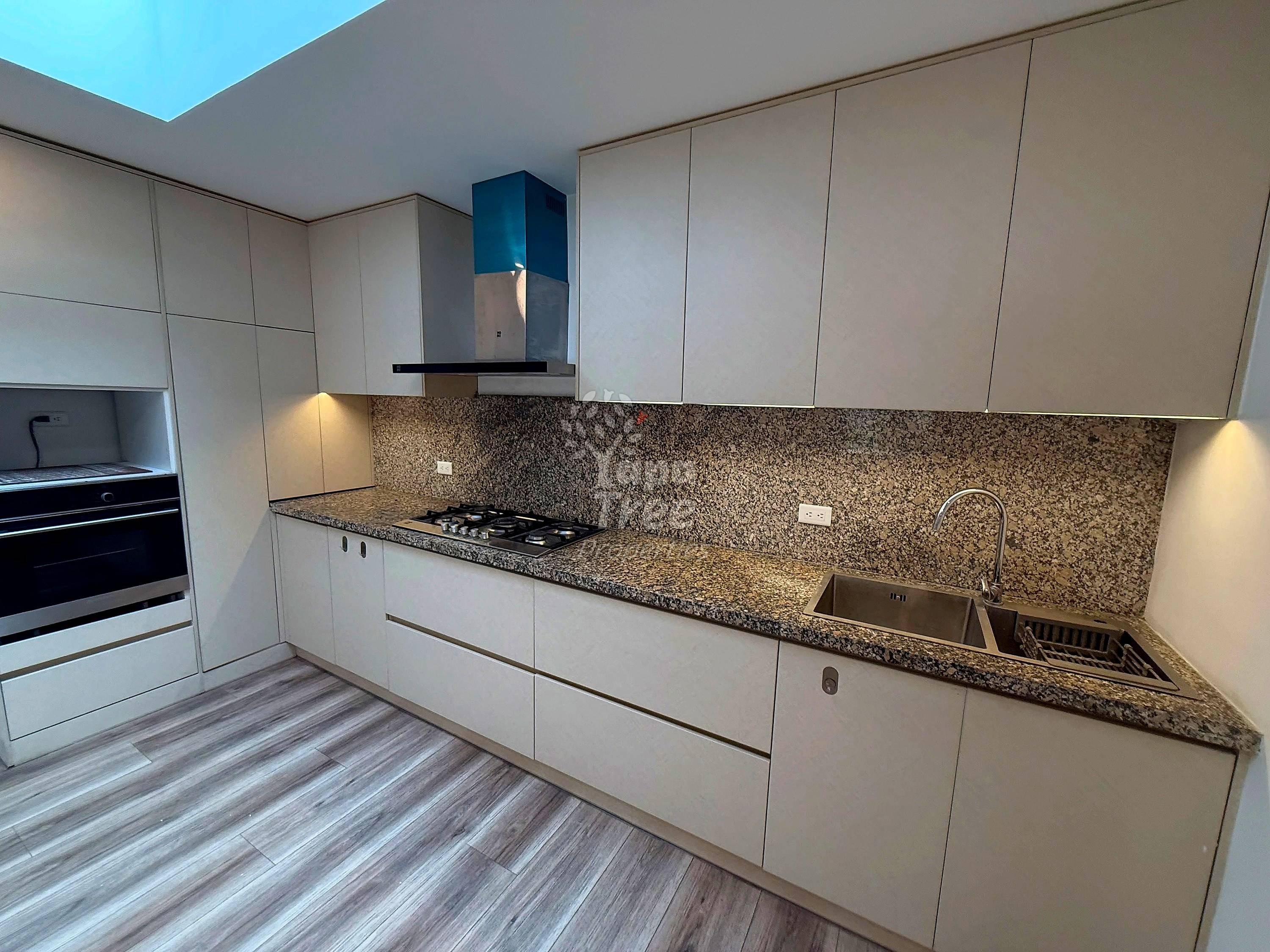 Modern kitchen with white cabinetry, granite countertops, gas cooktop, stainless sink, and skylight overhead.