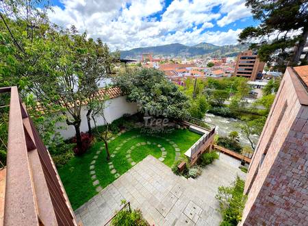 Overhead view of private courtyard with green lawn, stone pathway, trees, and brick boundary walls overlooking Cuenca cityscape and river.