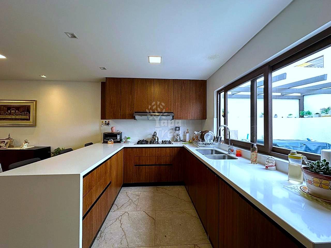 Modern kitchen with dark wood cabinetry, white countertops, stainless steel sink, gas cooktop, and large windows overlooking a terrace with recessed ceiling lights.