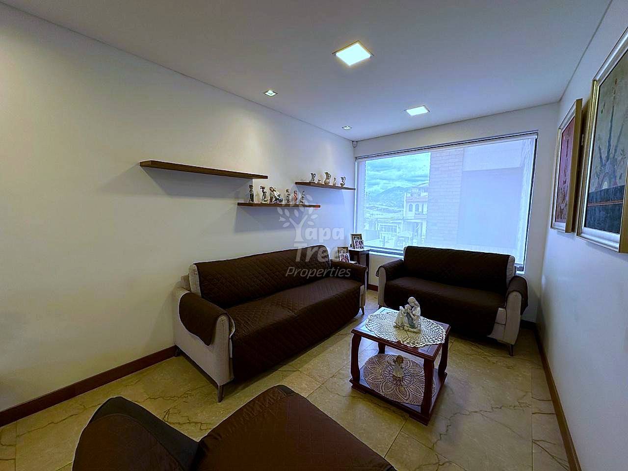 Living room with two dark brown and beige sofas, marble floor, wooden shelves, window with city view, and ceiling lights.