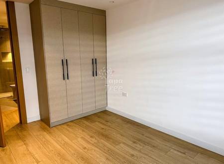 Bedroom with built-in four-door beige wardrobe, wooden plank flooring, white walls, and natural light from doorway.