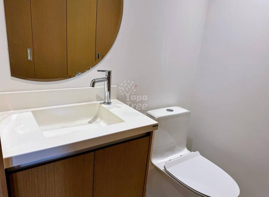 Bathroom with white walls, wood vanity cabinet, white countertop sink with chrome faucet, curved wood mirror cabinet, and white toilet.