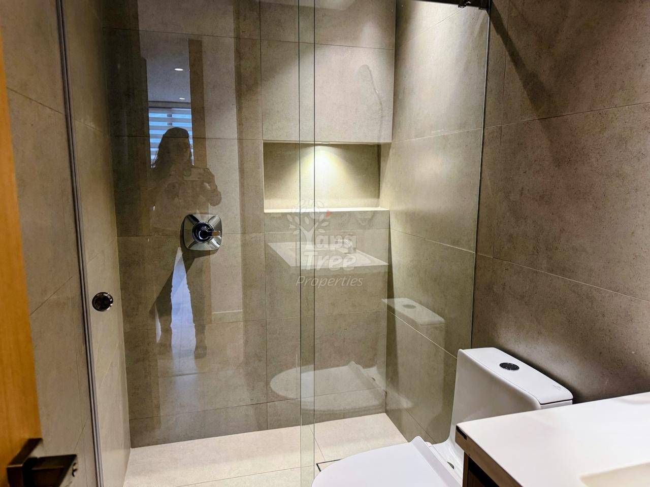Bathroom with large glass shower enclosure, beige tile walls, white sink vanity, and toilet visible on right side.