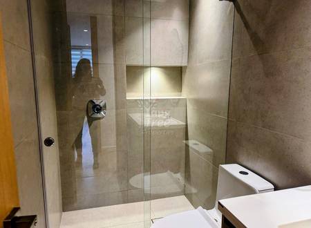 Bathroom with large glass shower enclosure, beige tile walls, white sink vanity, and toilet visible on right side.
