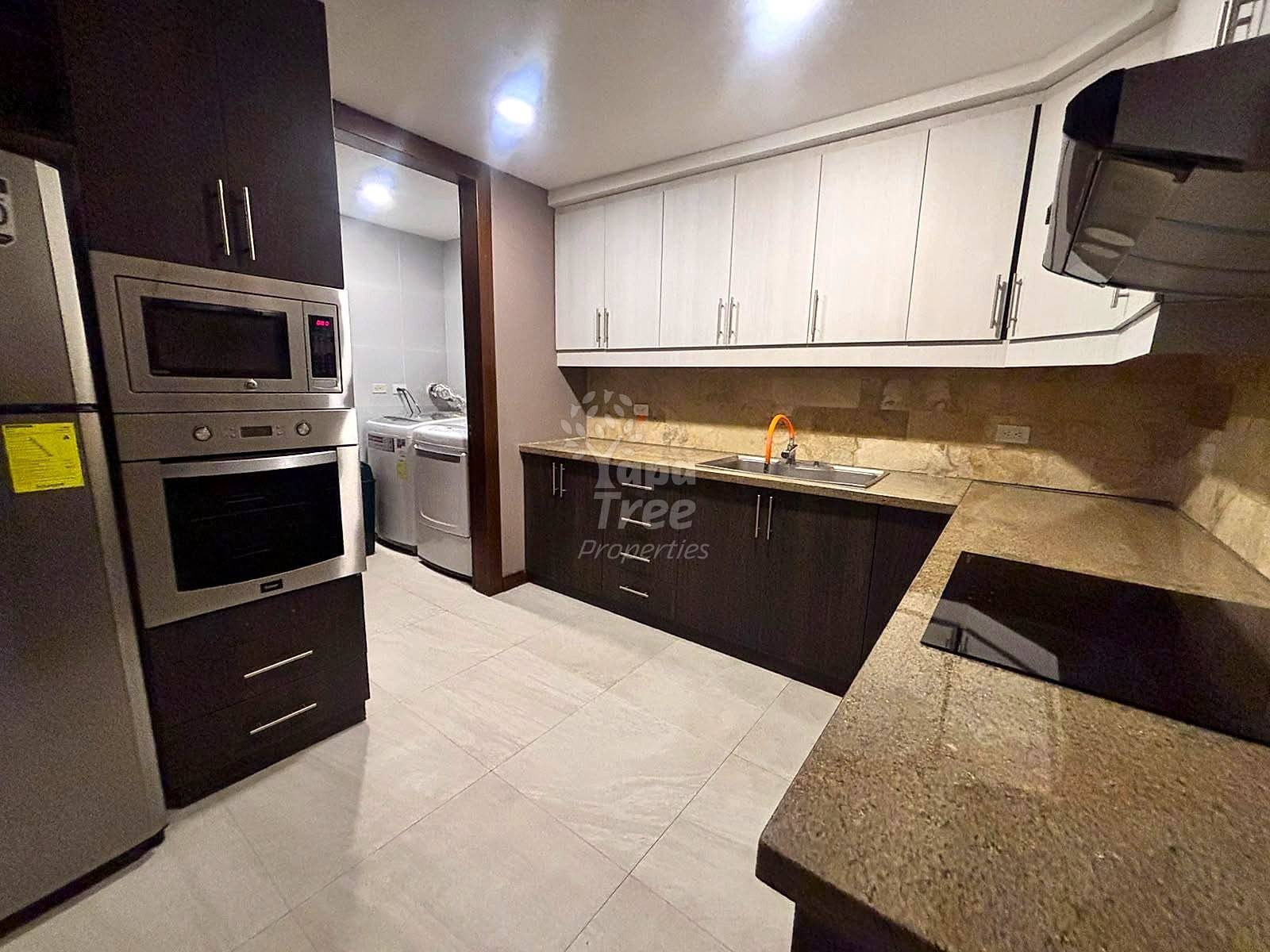 Modern cocina with dark wood cabinetry, granite countertops, stainless steel appliances, and white ceramic tile flooring throughout.