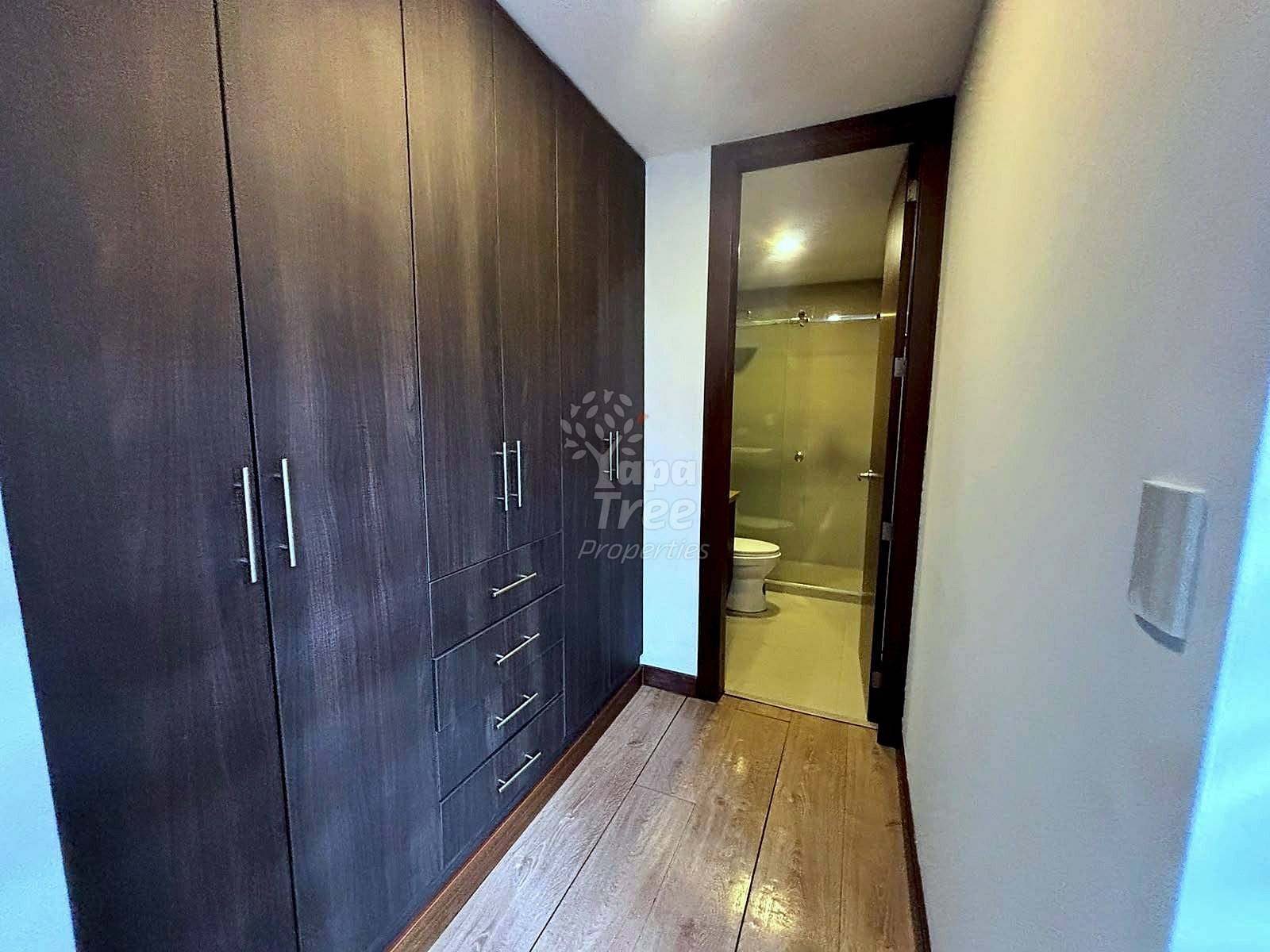 Bedroom hallway with dark wood wardrobe cabinets, wooden flooring, and open bathroom door with toilet visible.
