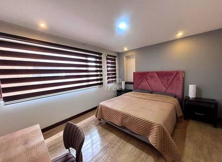 Bedroom with queen bed, burgundy upholstered headboard, wood nightstand, striped roller blinds, recessed ceiling lights, and wood-look flooring.