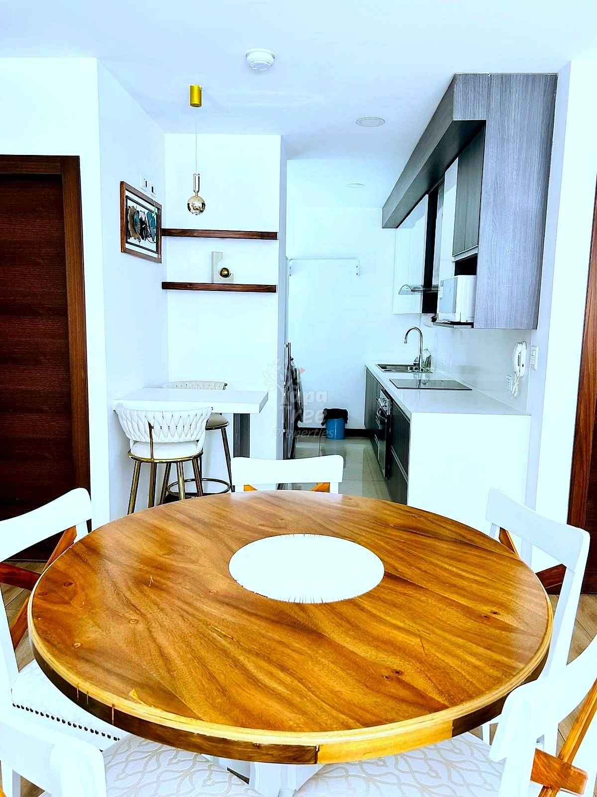 Open kitchen and dining area with round wooden table, white chairs, white cabinetry, stainless steel appliances, and pendant lighting.