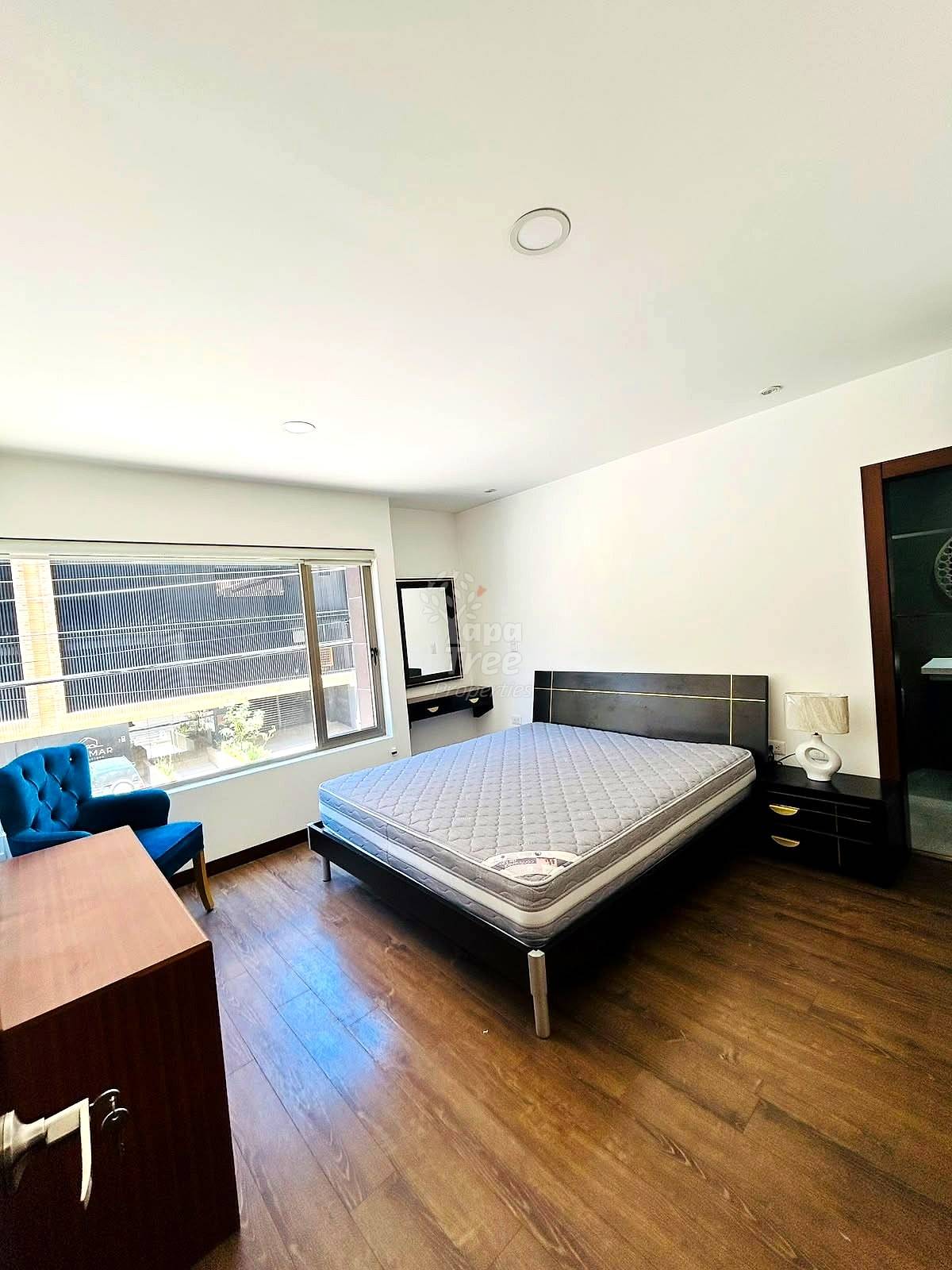 Bedroom with queen bed, black nightstands, blue chair, desk, wood flooring, large window, recessed lighting, and white ceiling.