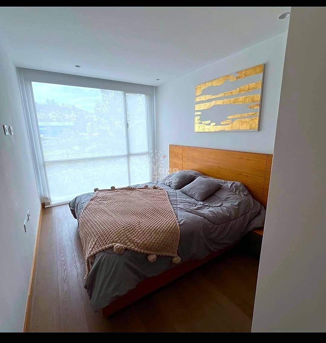 Bedroom with wooden bed frame, gray bedding, wood flooring, large sliding glass doors with city views, and abstract wall art.