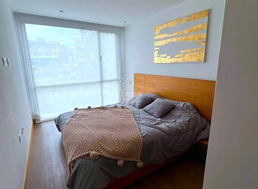 Bedroom with wooden bed frame, gray bedding, wood flooring, large sliding glass doors with city views, and abstract wall art.