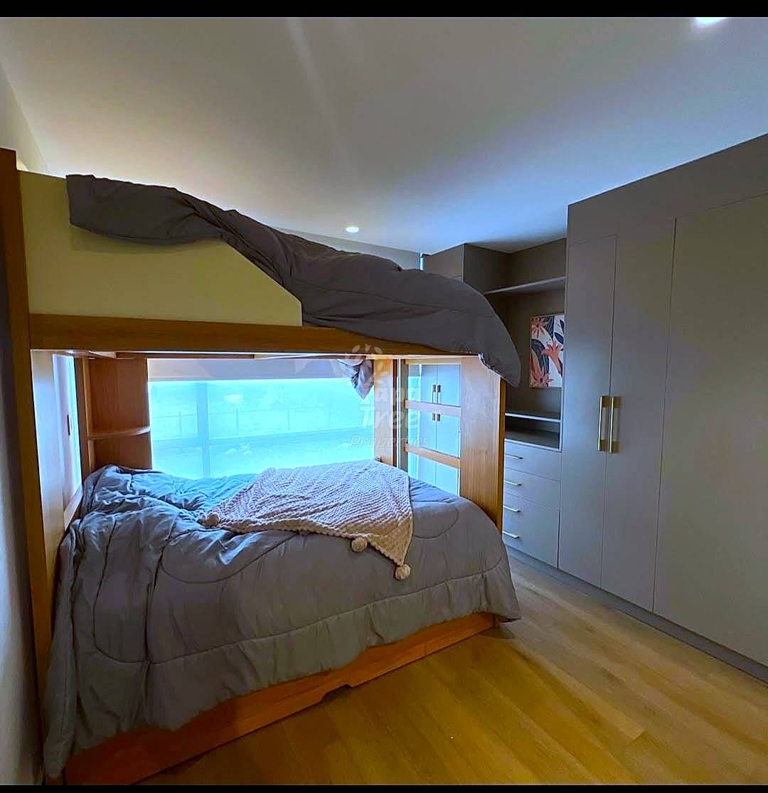 Bedroom with wooden built-in bed frame, gray bedding, large window with city view, recessed ceiling lights, and beige wardrobe storage on right wall.