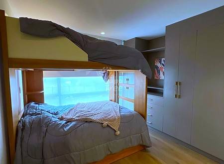 Bedroom with wooden built-in bed frame, gray bedding, large window with city view, recessed ceiling lights, and beige wardrobe storage on right wall.