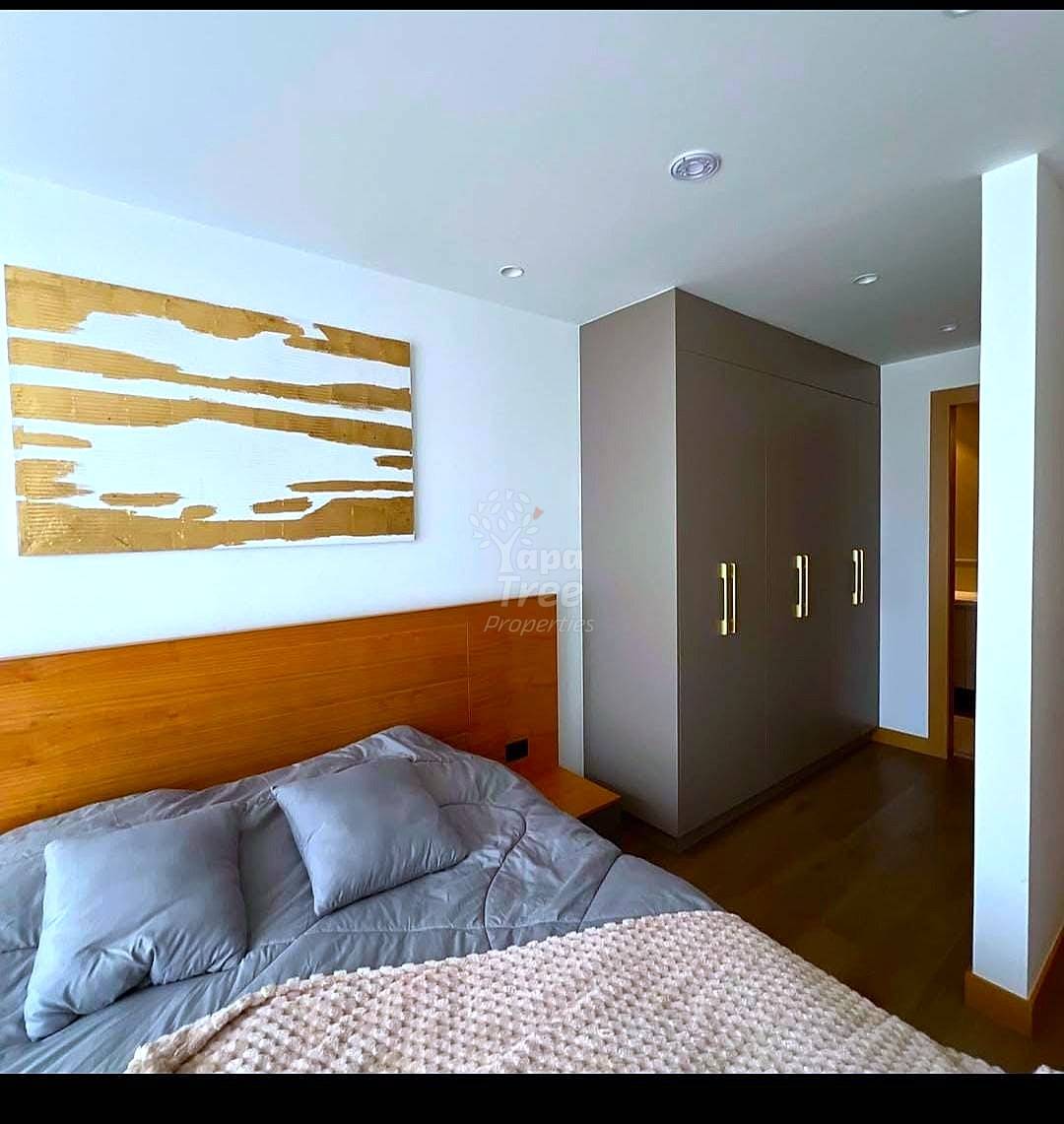 Bedroom with wooden bed frame, gray bedding, dark wood wardrobe with metal handles, and wooden wall art above bed.