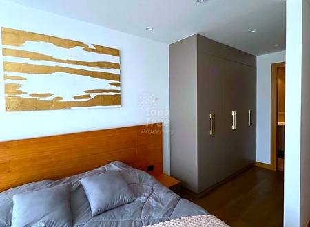 Bedroom with wooden bed frame, gray bedding, dark wood wardrobe with metal handles, and wooden wall art above bed.