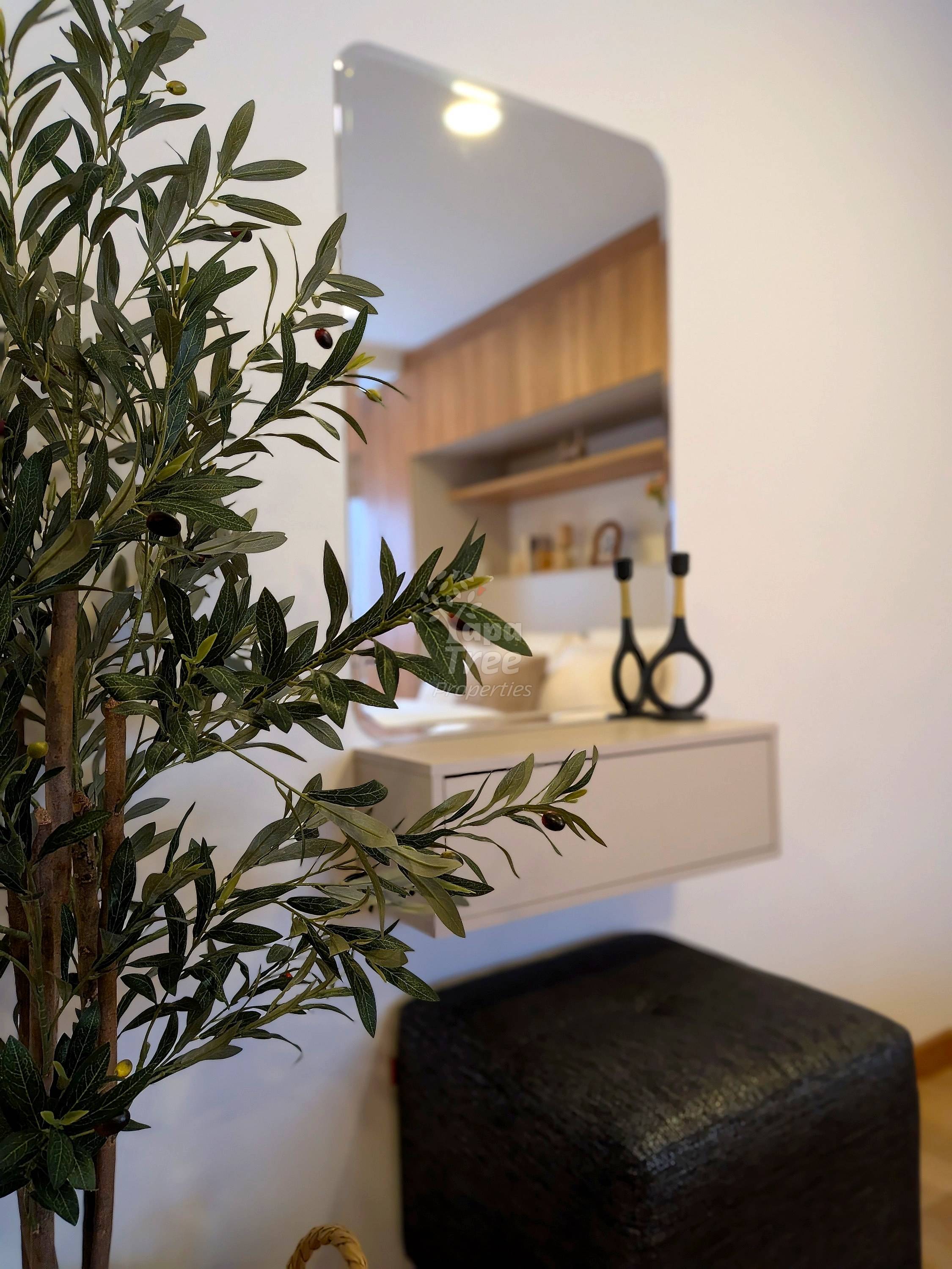 Modern bathroom with white vanity, mirror, potted plant, and black stool under warm lighting