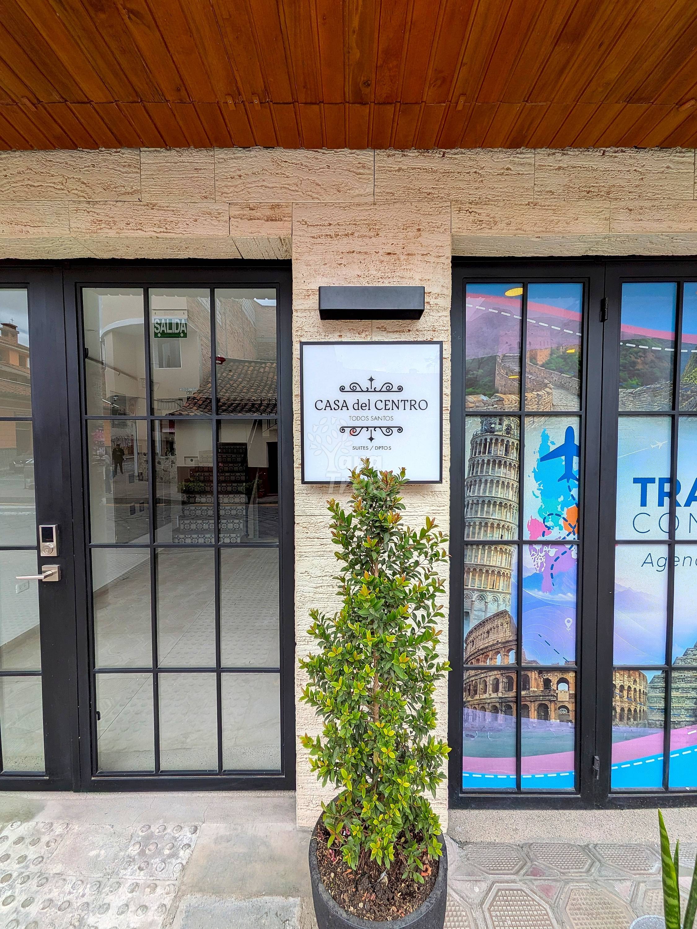 Storefront with travertine stone facade, wooden ceiling, black-framed glass doors and windows, and potted green plant.
