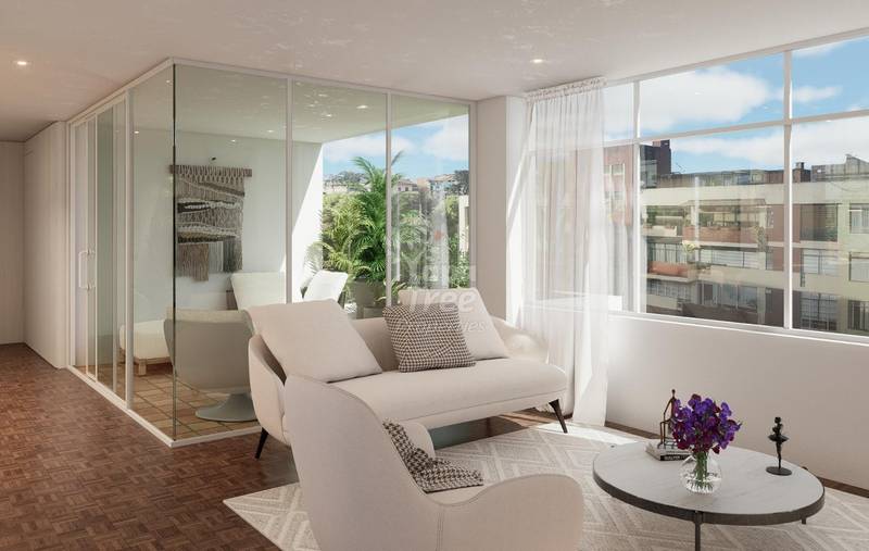 Modern departamento living room with cream sofa, glass-enclosed bathroom, large windows overlooking Cuenca cityscape, and terracotta tile flooring.