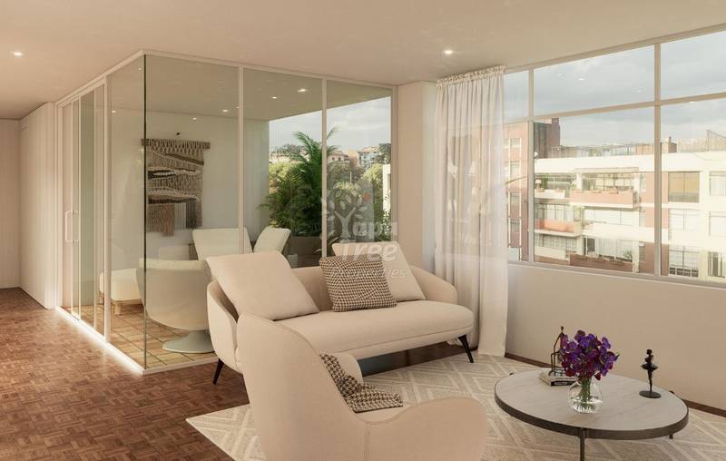 Modern living room with cream-colored seating, wood flooring, large windows overlooking city buildings, and glass-enclosed spa area with plant.