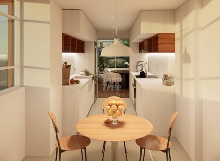 Modern galley cocina with round wooden dining table, two chairs, white cabinetry, dark wood upper cabinets, pendant light, and view into living area.