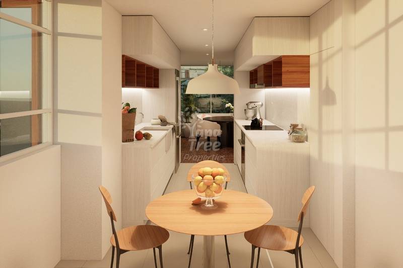 Modern galley cocina with round wooden dining table, two chairs, white cabinetry, dark wood upper cabinets, pendant light, and view into living area.