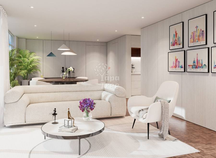 Modern living room with cream curved sofa, white armchair, round white coffee table, pendant lights, wooden dining table, potted plant, and framed cityscape artwork on light walls.