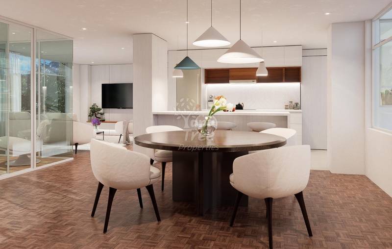 Open-concept dining and kitchen area with round dark wood table, cream upholstered chairs, pendant lighting, and modern white cabinetry with wood accents.